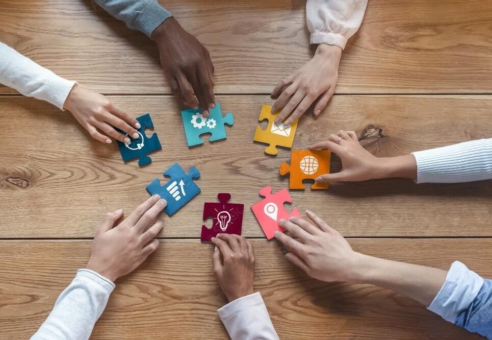 A group of people sitting around a table with puzzle pieces.